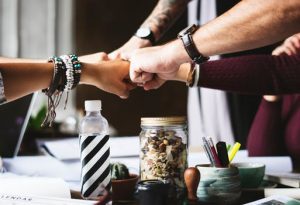 A photo of about five people doing a fistbump over a desk.