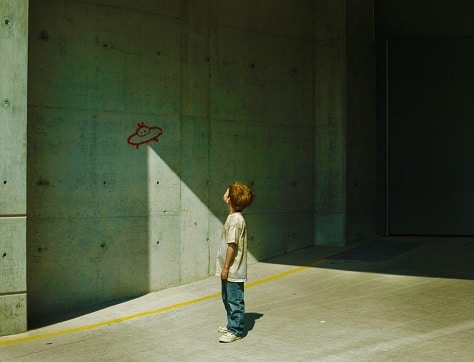 An illustration of a boy looking at a drawing of an alien spaceship on a wall