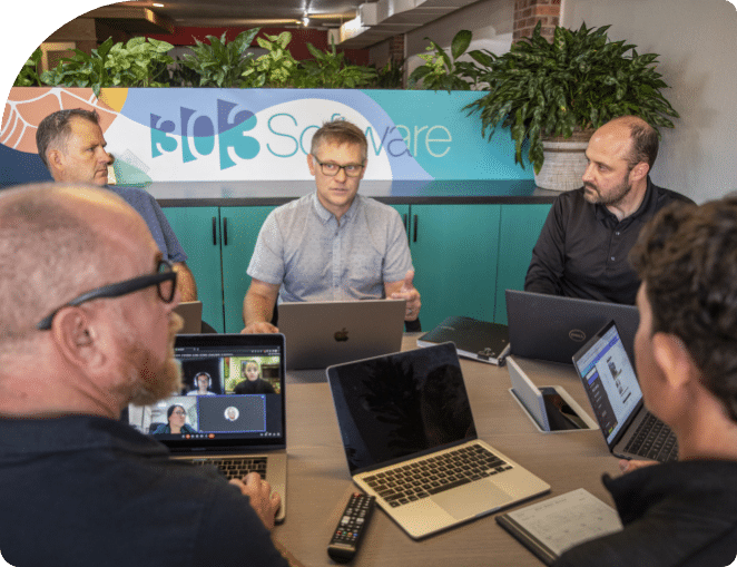 A group of employees sitting around a table with laptops during a boardroom meeting in Denver, Colorado.